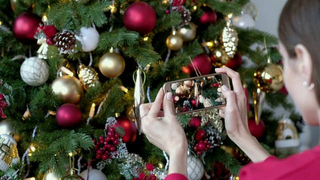 女性在家用智能手机拍照装饰圣诞树。圣诞、寒假与人观念。视频下载