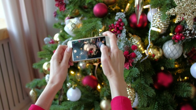 漂亮的女人在智能手机上拍摄圣诞树和家里的玩具。圣诞、寒假与人观念。视频下载