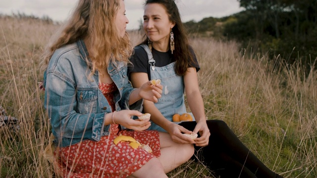 两个年轻的女人坐在田野里，吃着新鲜的橘子野餐视频素材