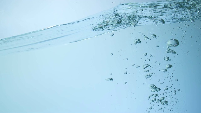 慢镜头近距离的一个强大的水波碰撞在水池与3个冰块落在蓝色的背景视频素材