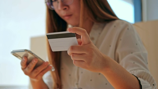 年轻的亚洲女子在网上购物用手机和信用卡在咖啡馆视频素材