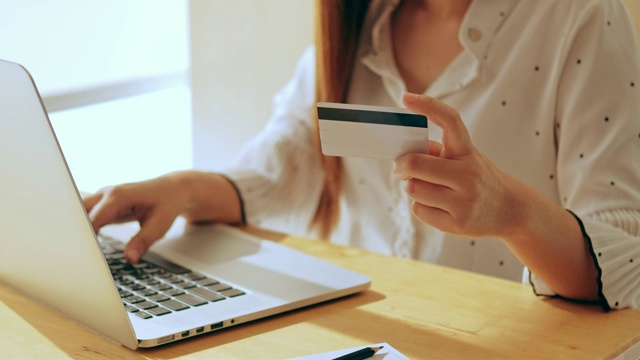 年轻的亚洲女子在网上购物与笔记本电脑和信用卡在咖啡馆视频素材