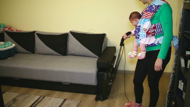 家庭主妇抱着婴儿用吸尘器打扫房间视频素材