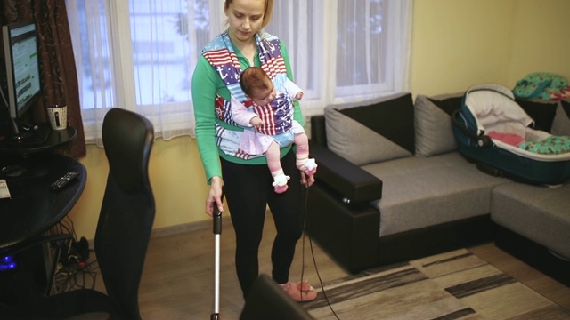 家庭主妇抱着婴儿用吸尘器打扫房间视频素材