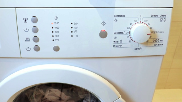 女人的手合上洗衣机，打开一个洗涤程序，按下前面板上的一个按钮视频素材