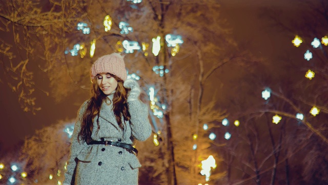 美丽的女孩在夜晚走在冬天的小路上。街上灯火通明。自底向上的视图。视频下载