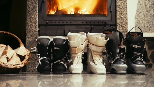4K静态镜头三双滑雪靴站在壁炉旁边。寒假的概念。视频下载