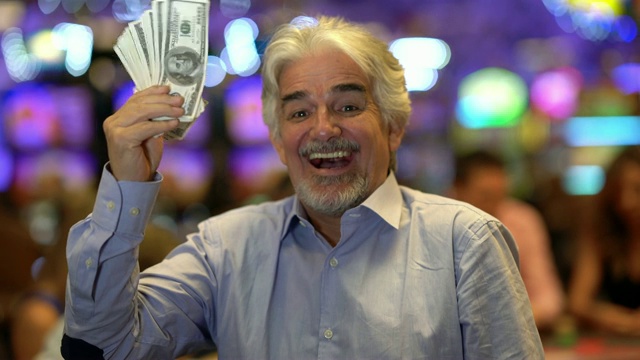 拉丁美洲的老人拿着一堆钱，看着和笑在赌场的相机视频素材