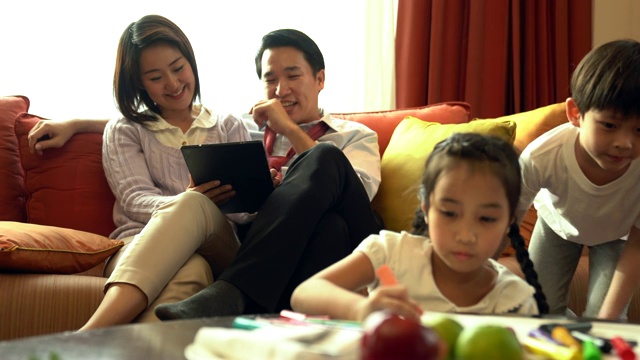 幸福的家庭一起在客厅度过时光。儿童着色和家长看平板电脑在背景。视频素材