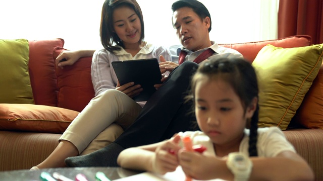 幸福的家庭一起在客厅度过时光。儿童着色和家长看平板电脑在背景。视频素材