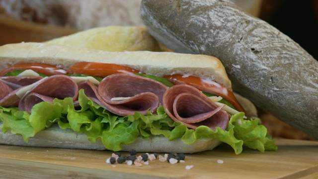 面包卷和金枪鱼三明治，红洋葱，沙拉和黄瓜片，在一张木桌上移动的静态镜头。视频素材
