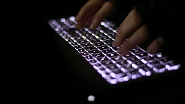 一名男性黑客在暗室里操作一台电脑，电脑屏幕上显示着数据视频下载