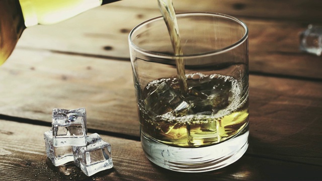 将威士忌从瓶子中倒入装有冰块的玻璃杯中视频素材