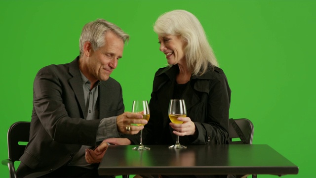 一对情侣坐在模糊的背景前，在绿色屏幕上喝香槟视频素材