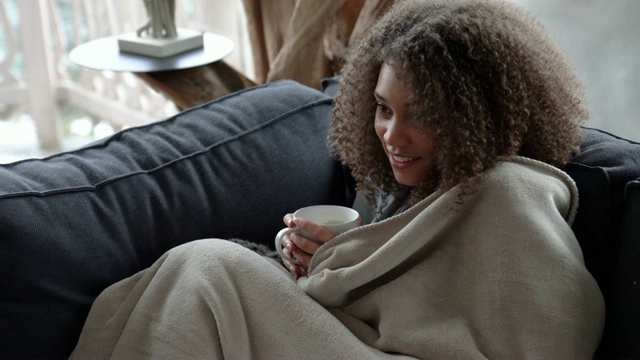看电视的女人用毯子盖着自己，在寒冷的冬天的早晨喝咖啡视频素材