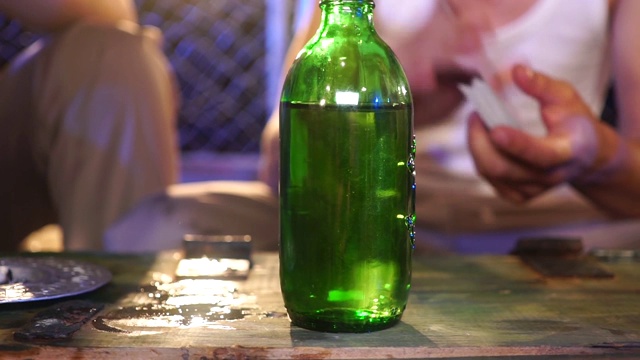 在一个绿色瓶子后面，一个穿着白色t恤的人正在洗牌，然后在旧木箱上玩视频下载