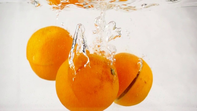 劈开的橙子迅速沉到带气泡的水中，慢镜头特写视频素材