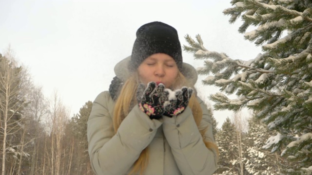 年轻的女孩手里拿着雪。女孩在冬天的森林里吹起雪花视频素材