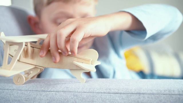 男孩玩木制飞机玩具模型的镜头。他把它“落地”在客厅的沙发扶手上。视频素材