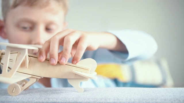 男孩玩木制飞机玩具模型的4K视频。他把它“落地”在客厅的沙发扶手上。视频素材