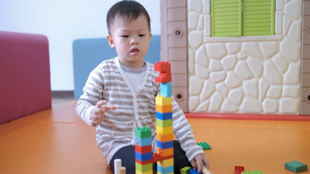 可爱的小亚洲2 - 3岁的蹒跚学步的男孩在室内玩五颜六色的塑料积木视频下载