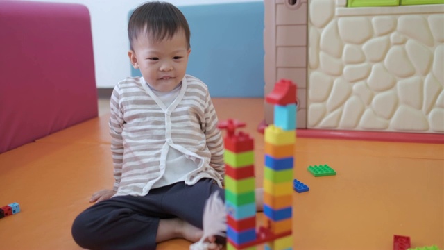 可爱的小亚洲2 - 3岁的蹒跚学步的男孩玩彩色塑料块的乐趣视频素材