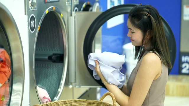 一个漂亮的女人正在自动洗衣店洗衣服。视频下载