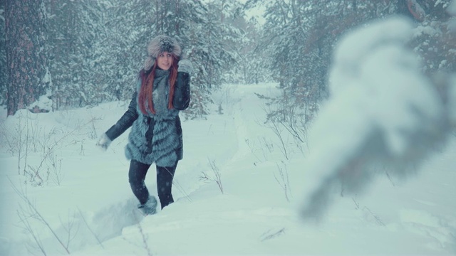美丽的女孩走在森林中雪堆之间的小路上。雪落。视频下载