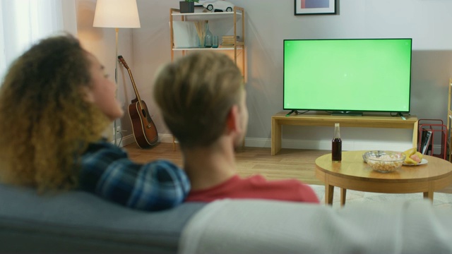 一对幸福的夫妇坐在家里看绿色屏幕，放松在沙发上。看体育比赛，新闻，情景喜剧电视节目或电影。视频素材