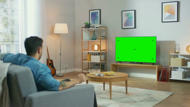 在客厅:一个人放松在沙发上看绿色屏幕电视。视频素材