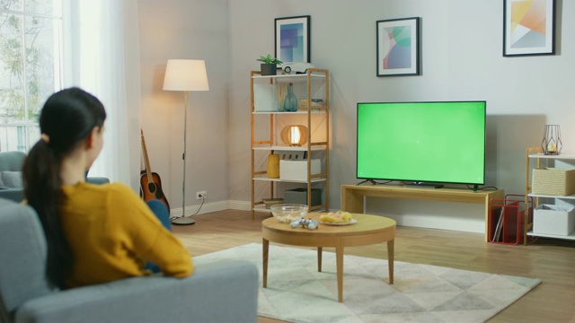 女孩坐在家里的沙发上，看着绿色屏幕，放松。男人在舒适的房间里看体育比赛，新闻，情景喜剧电视节目或电影。视频素材