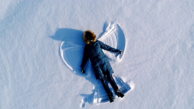 女人在雪地里做了一个雪天使。航拍视频。相机慢慢移开。视频下载