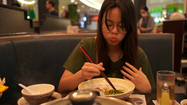 年轻的亚洲妇女用筷子吃食物，素喜烧，涮涮锅视频下载