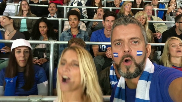 一名男子穿着球迷服装，用智能手机拍下了他和女友在体育场欢呼的视频视频素材