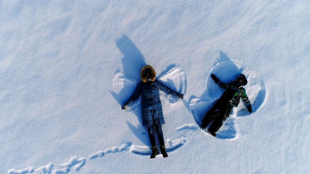 妈妈和儿子一起做雪天使。镜头缓慢上升。空中镜头。视频下载