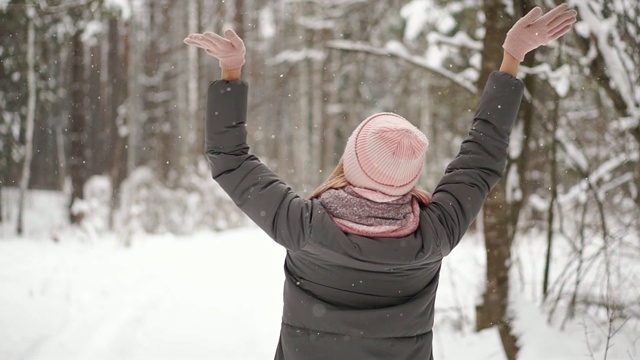 慢镜头，一个穿着夹克、帽子和围巾的女人在冬天的森林里手里拿着雪，吹向镜头扔出雪来视频素材