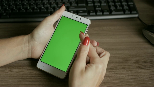 坐在办公桌前看绿色屏幕智能手机的女人。商务女性使用智能手机。4 k UHD。关闭了。视频素材