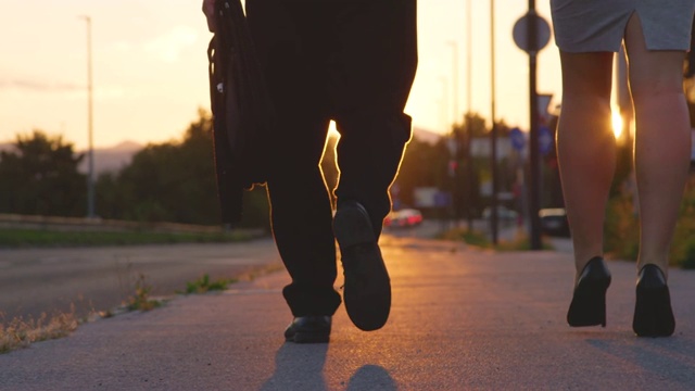 镜头光晕女孩穿着高跟鞋和她的同事走在夕阳下的人行道上视频素材