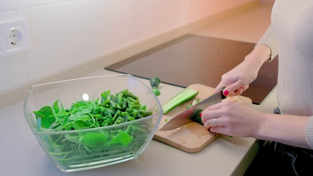 慢镜头，一个不认识的女人用一把菜刀在木板上切黄瓜。在前景是一个玻璃碗沙拉。健康食品和素食的概念视频素材