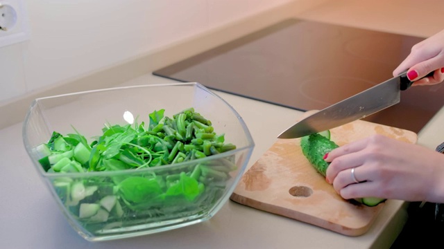 特写，慢镜头，一个不认识的女人用一把大菜刀在木板上切黄瓜。在前景是一个玻璃碗沙拉。健康食品和素食的概念视频素材