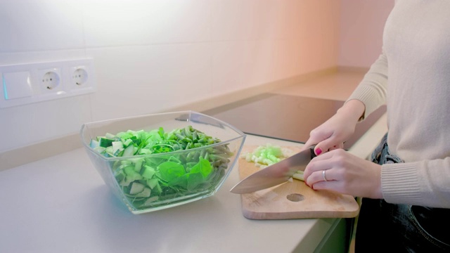慢镜头，一个不认识的女人用一把大菜刀将一块木板上的芹菜切进一个玻璃沙拉碗里。饮食和素食的概念视频素材