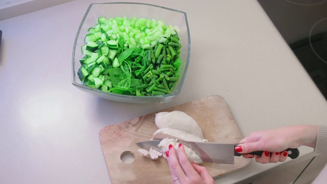 特写，慢镜头，不认识的女人用一把大菜刀在玻璃沙拉碗里的木板上切鸡肉片。自制饮食和素食的概念视频素材