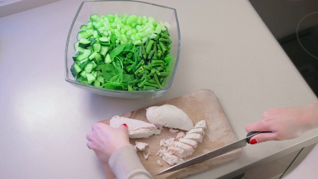 特写，慢镜头，一个不认识的女人用一把大菜刀在一个玻璃沙拉碗的木板上把鸡柳切成小块。自制饮食和素食的概念视频素材