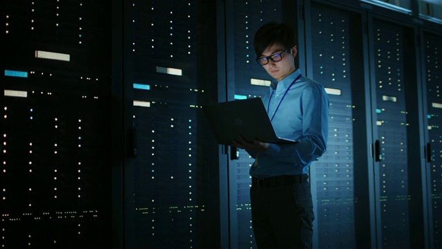 在黑暗的数据中心:男性IT专家走在一排操作服务器机架上，使用笔记本电脑进行维护。云计算、人工智能、超级计算机、网络安全的概念视频素材