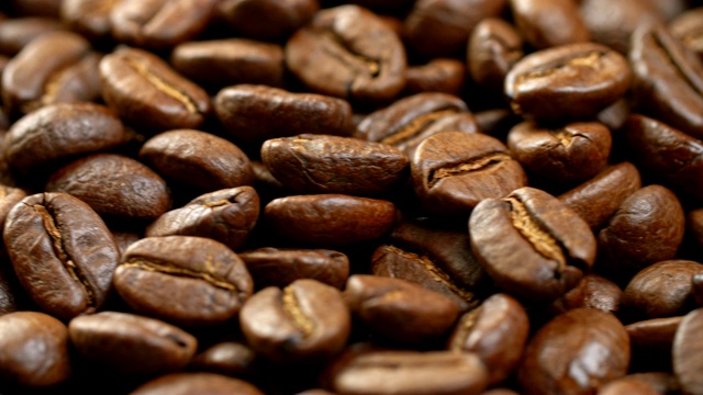 咖啡豆的背景。一个旋转面板的特写，充满了棕色烤可口的咖啡豆。4 k视频素材