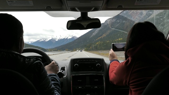 快乐的夫妇开车和使用手机拍照在乡村公路在冬天，旅行视频购买
