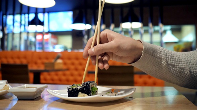 在一家日本餐馆里，一对年轻夫妇用筷子从盘子里拿寿司。视频素材