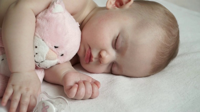 一个可爱的新生女婴和一个柔软的粉色猫咪玩具睡觉的特写视频素材