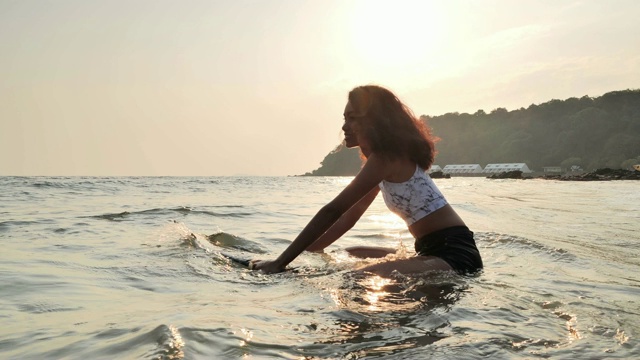 美丽的年轻女子坐在冲浪板上等待海浪。体育cinemagraph视频素材