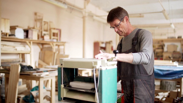 专业成熟的木工在自己的木工车间里用木工机械打磨木板视频素材